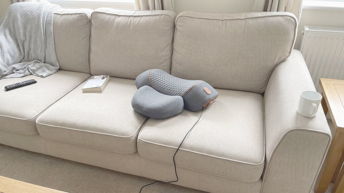 The FisioRest sitting askew on a cushion of a family sofa, its single cable trailing off the front, a throw, a remote and a mug around it.