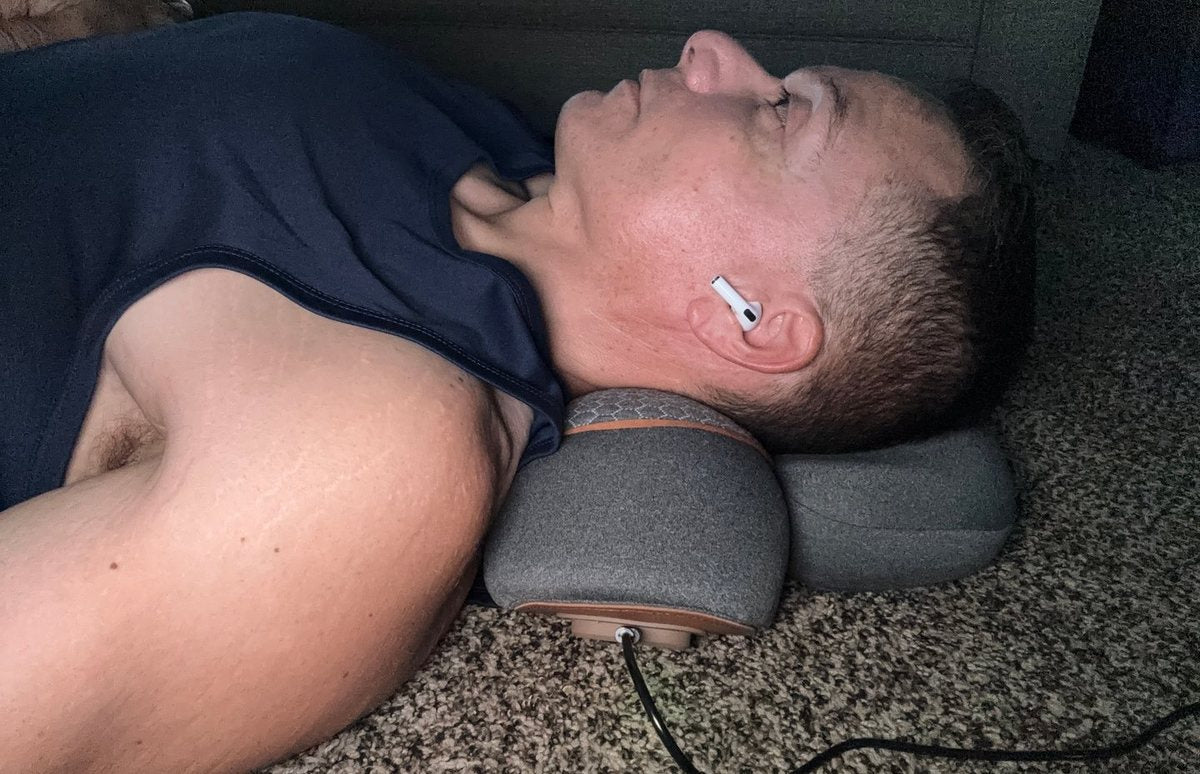 A customer photograph of a man lying back with the FisioRest tipping his head back, eyes closed.