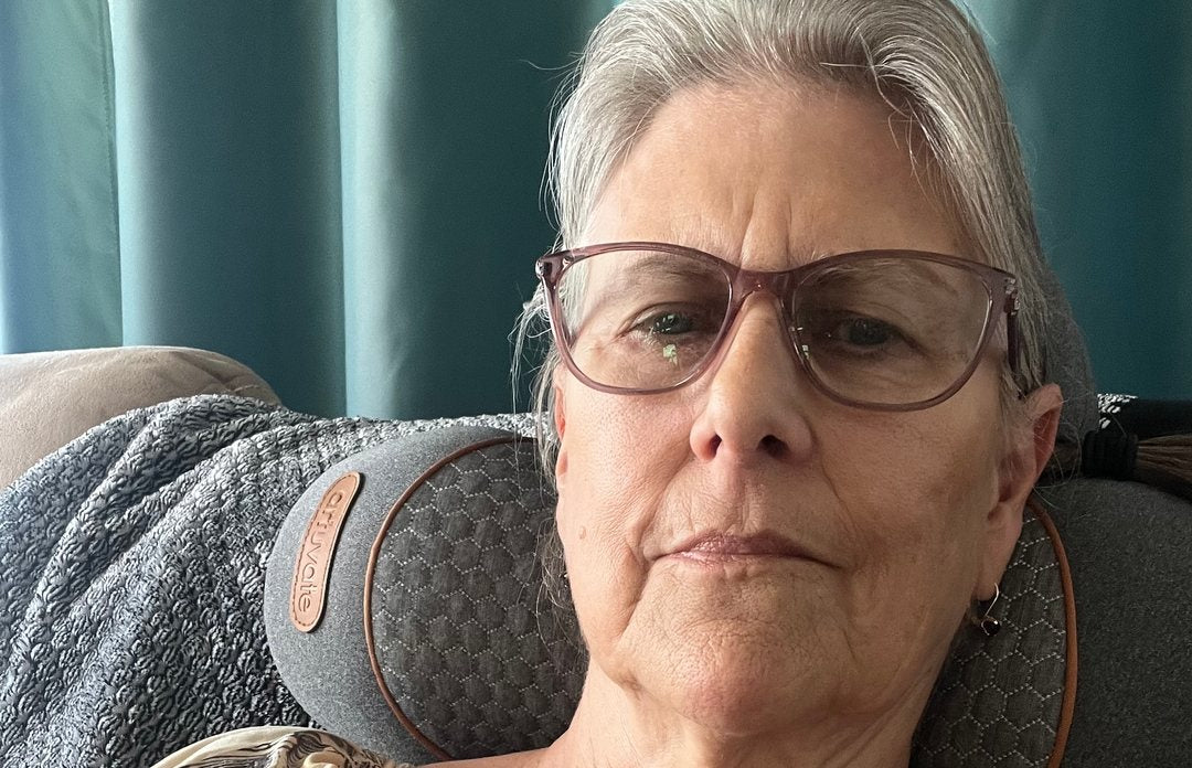 A customer photograph of an older woman relaxed in an armchair with the FisioRest behind her neck.