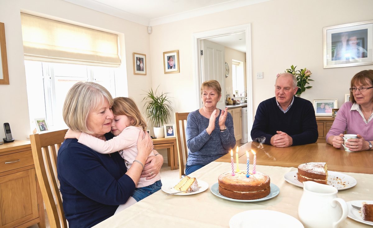A family snapshot at the birthday table, the narrator holding her granddaughter close with both arms round her, four candles lit on the cake.